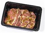 Marinated pork neck steaks in plastic container