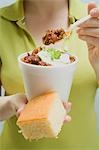 Woman holding chili con carne in paper cup and cornbread