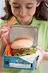 Little girl holding lunch box containing burger & carrots