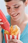 Young woman squeezing ketchup out of bottle onto chips