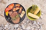 Meat & vegetables on barbecue, accompaniments in bowl