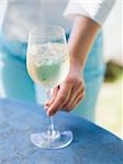 Woman reaching for glass of white wine with ice cubes on table