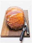 Glazed ham on chopping board with carving cutlery