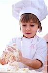 Little girl in chef's hat kneading dough