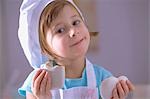 Little girl in chef's hat eating heart-shaped gingerbread