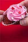 Taking chocolate cupcake with pink icing out of paper case