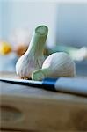 Two fresh garlic bulbs on chopping board with knife