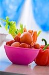 Tomatoes in a pink coloured bowl with peppers, carrots and celery