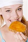 Young woman with headscarf biting into a slice of bread with apricot jam