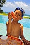 Garçon avec des lunettes de natation sur tête manger la pizza sur la plage
