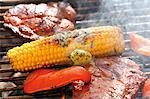 Corn on the cob with herb butter, pork steaks & pepper on barbecue
