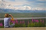 Jeune femme est assise sur le sol à la recherche au moyen de jumelles Regarde un Mt McKinley et la chaîne de l'Alaska l'Alaska Denali National Park