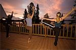 Frauen üben Sie Yoga bei Sonnenaufgang auf dem Deck der Winter Lake Lodge. Sommer in South Central Alaska.