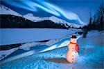 Lighted snowman decoration standing on riverbank Alaska Winter Composite