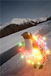 Plastic penguin wrapped in Christmas tree lights sitting on riverbank Winter Alaska