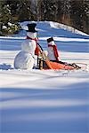 Large pushes small snowman on dog sled in deep snow in afternoon Fairbanks Alaska winter