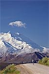 Two women ride bikes over Thorofare Pass with Mt. McKinley in the background in Denali National Park, Alaska