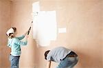 Couple using paint rollers on interior room