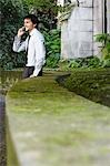 Businessman on cell phone leaning against wall in park