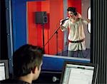 Young woman singing in studio, technician in foreground