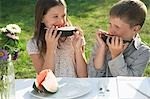 Boy and girl (7-9) sitting at table in garden and eating watermelon