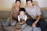 Couple sitting on sofa, Watching Television while son is using remote control