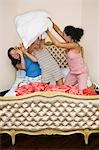 Teenage Girls pillow fighting, kneeling on funky bed