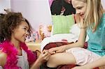 Young girl applying nail polish to friends finger in bedroom