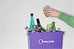 Person putting jar into recycling container filled with empty glass vessels