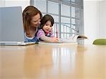Fille (3-4) à colorier livre à côté de la mère à l'aide d'ordinateur portable, dans la maison
