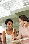 Two businesswomen in conference meeting, one using mobile phone
