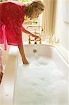 Femme en peignoir se penchant vers le bas sur la baignoire remplie de bulles, tester l'eau, vue latérale