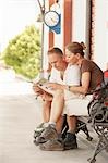 Hiking couple looking at map, sitting on railway platform