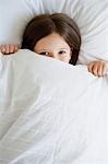 Little girl in bed pulling covers over face, portrait, high angle view