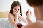 Mother giving cough syrup to reluctant daughter in bedroom