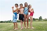 Two young girls and boys in swimsuits in field holding water pistols, portrait