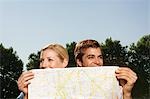 Lost smiling young couple in park holding map