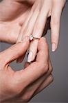 Man placing engagement ring on woman's finger, close-up of hands