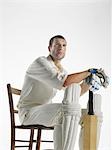 Cricket player sitting in chair, holding cricket bat, side view