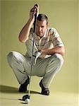 Golfer squatting, holding golf club and squinting