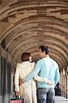 Couple with arms round each other walking through archway, back view