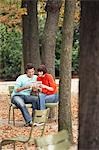 Couple reading guide book, sitting on chairs, in park