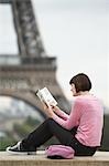 France, Paris, Young woman reading book on balcony in front of Eiffel Tower