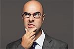 Bald businessman wearing glasses with hand on chin, making funny face