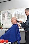 Barber shaving mans head in barber shop