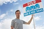 Man holding sold sign, against sky