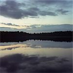 Sky and trees reflected in lake at night