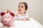 Baby boy sitting in highchair with piggy bank and coins