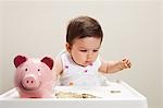 Baby boy sitting in highchair with piggy bank and coins