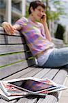 Jeune femme avec un téléphone portable, iPad, journaux et magazine sur un banc